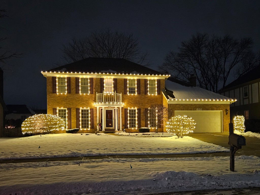 Brick home with warm white window frames and lit bushes